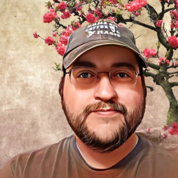 A picture of yours truly, the author. It's me in a brown t-shirt, wearing a hat that says this mom runs on magic and fairies. Behind me is the image of a sakura tree.