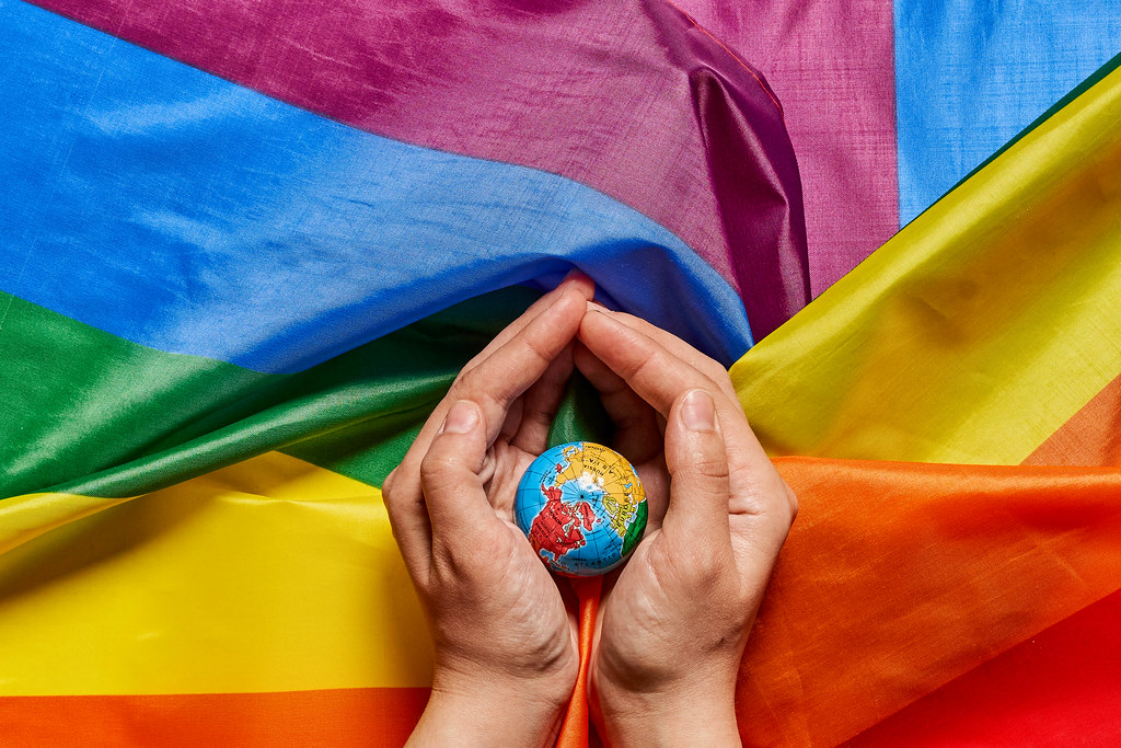 a small globe of the Earth cupped by a person's hands on top of a rainbow flag.