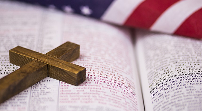 A small wooden cross sits on top of an open Bible.