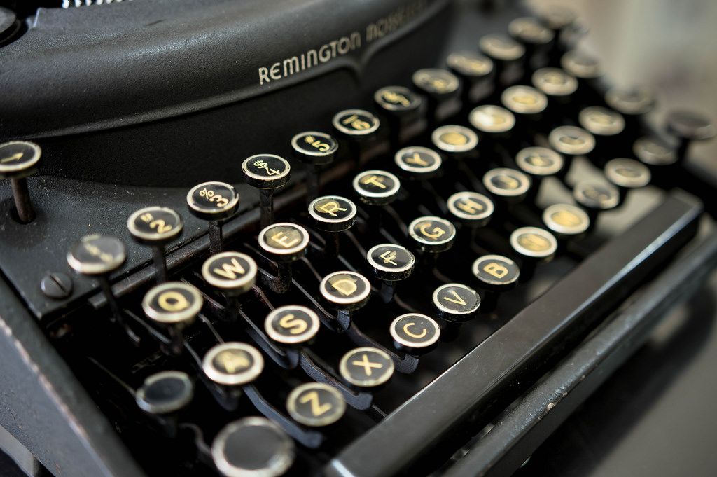 An image of an old typewriter, a Remington, black with brass and white keys. 