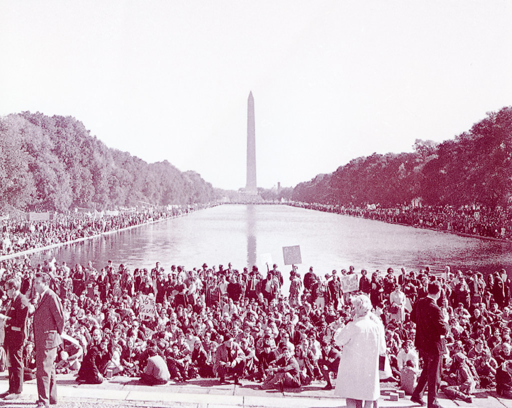 An image of an anti-war march at the US capitol, in front of the Washington monument. Various protestors are carrying signs against the war.