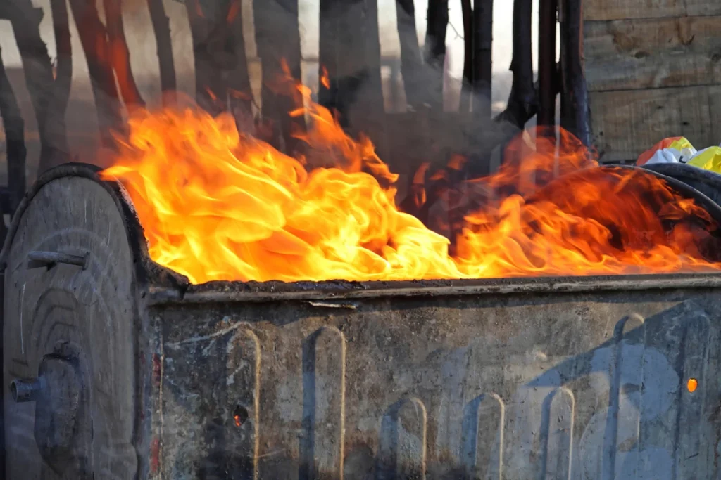 An image of a blue dumpster, charred all around the edges and on fire.